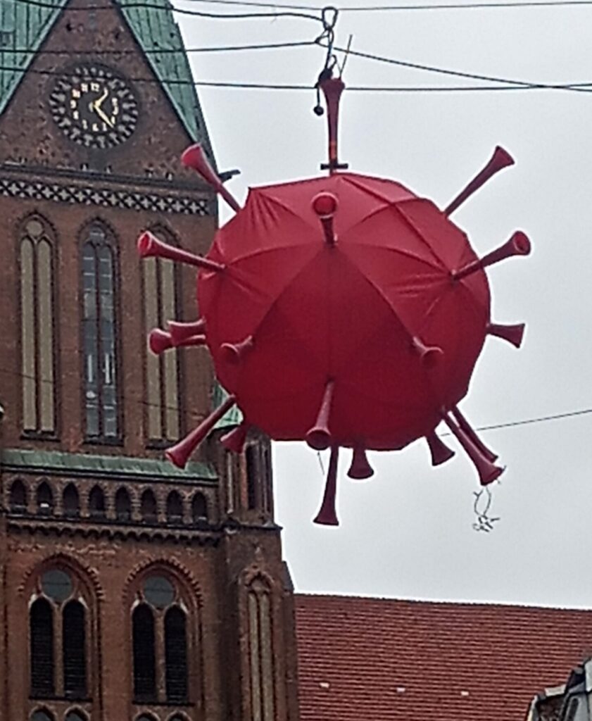 roter Coronavirus als Ballon vor einem Kirchturm